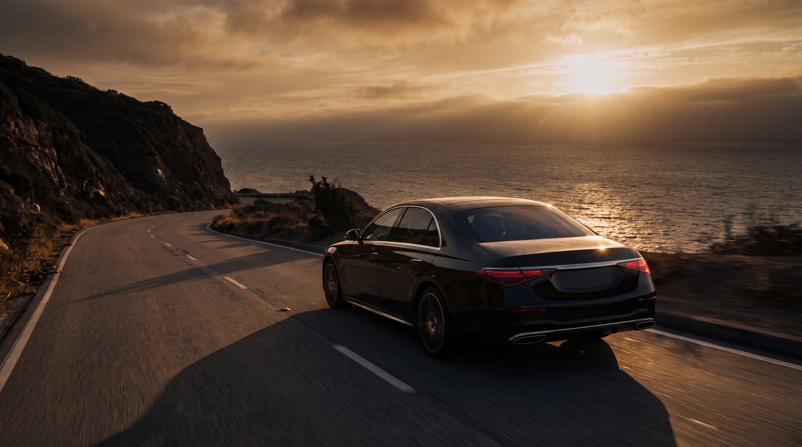 A VOGA luxury sedan glides along a coastal road toward a low amber sun.